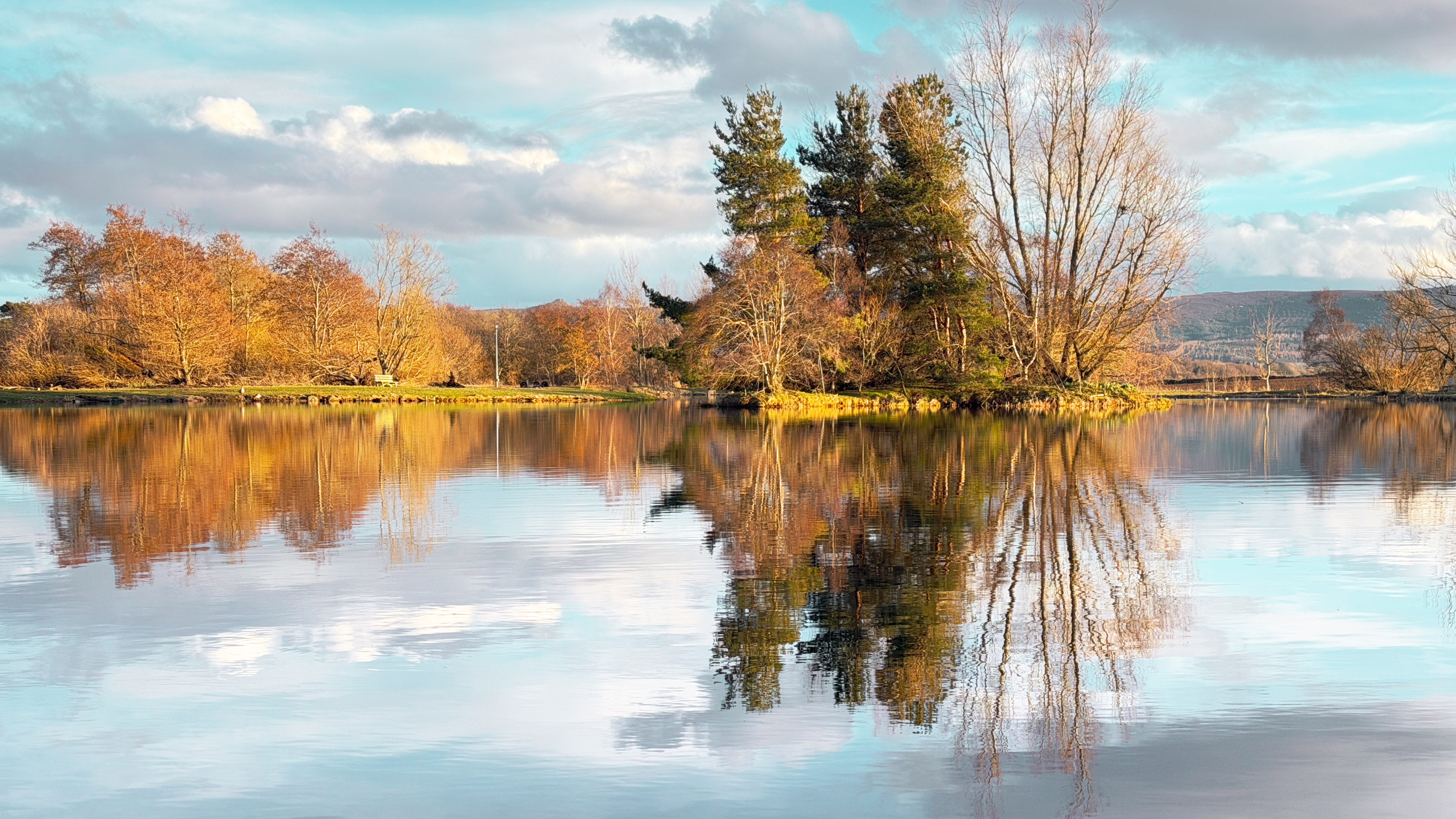 Autumn trees and island perfectly reflected in the still surface of Loch Insch